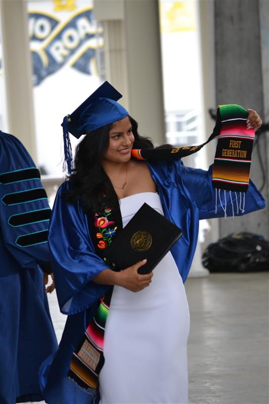 graduate holds up scarf that says "First Generation"
