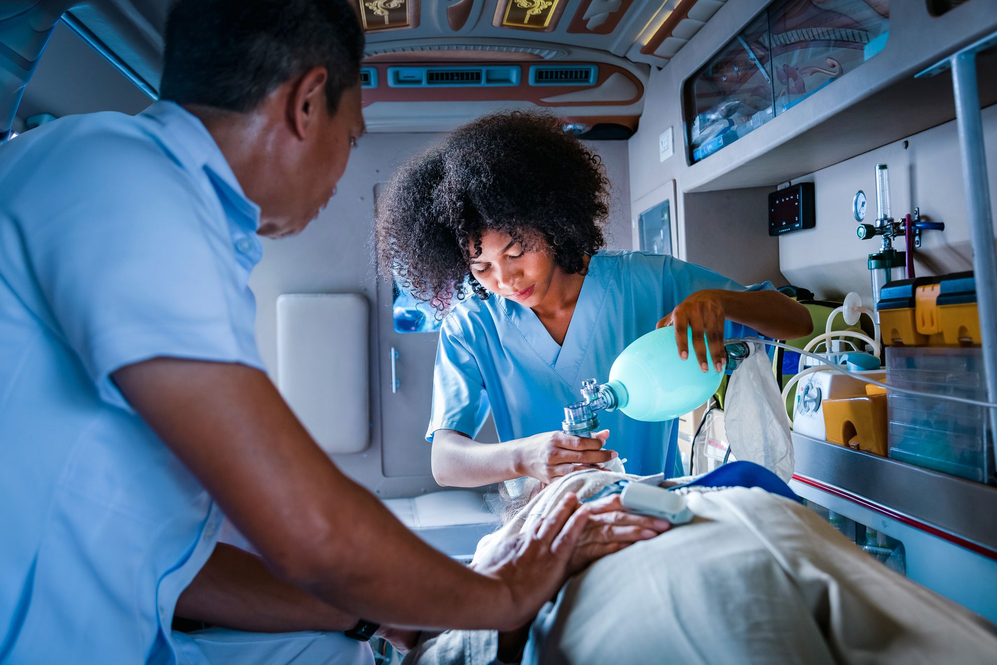 two paramedics help patient with breathing machine in ambulance